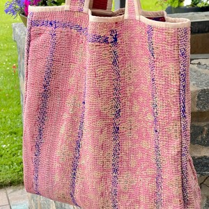 K&ouml;nnte beinhalten: Eine rosafarbene und blaue Kantha-Tragetasche mit floralem Muster. Die Tasche hat einen langen Riemen und ist aus recyceltem Stoff gefertigt.
