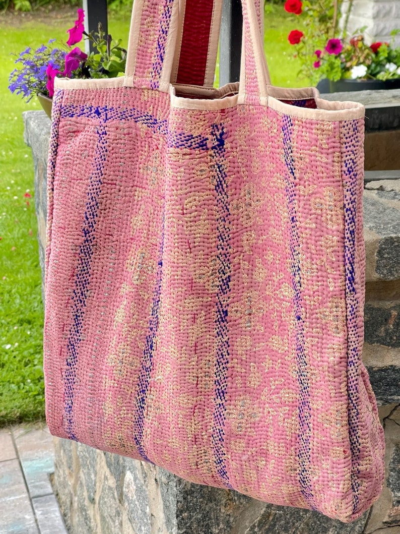 K&ouml;nnte beinhalten: Eine rosafarbene und blaue Kantha-Tragetasche mit floralem Muster. Die Tasche hat einen langen Riemen und ist aus recyceltem Stoff gefertigt.