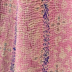 K&ouml;nnte beinhalten: Rosa Kantha-Steppdecke mit floralem Muster und blauen N&auml;hten. Die Decke ist aus Baumwolle und hat ein weiches, handgen&auml;htes Gef&uuml;hl.