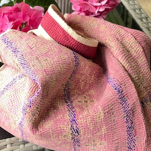 K&ouml;nnte beinhalten: Rosa gesteppte Tragetasche mit einem wei&szlig;en und roten Riemen. Die Tasche hat ein Blumenmuster und blaue N&auml;hte.