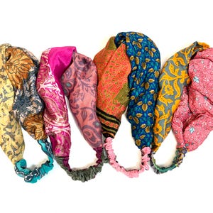 Könnte beinhalten: Fünf farbenfrohe Stirnbänder mit Gummibändern. Die Stirnbänder weisen verschiedene Muster und Farben auf, darunter Blumen- und Paisley-Designs in Gelb-, Rosa-, Orange- und Blautönen. Die Gummibänder sind in passenden Farben gehalten.