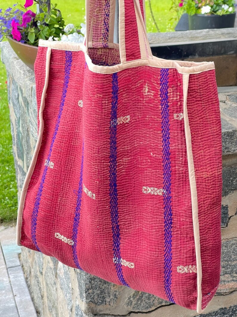 K&ouml;nnte beinhalten: Eine rot-blaue gestreifte Tragetasche mit cremefarbenem Besatz. Die Tasche ist aus gestepptem Stoff und hat ein einzigartiges, handgen&auml;htes Design.