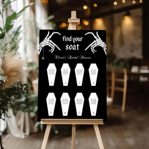 May include: Black and white printable seating chart with a spooky Halloween theme. The chart features a skeleton hand pointing to the text "Find your seat" and a spider hanging from a web. The chart is divided into eight sections, each with a coffin-shaped space for a name. The text "Olivia's Bridal Shower" is at the top of the chart.