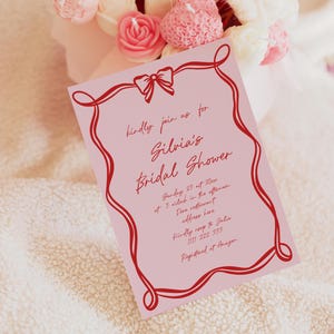 Può includere: Un invito rosa per un addio al nubilato con bordo decorativo e fiocco rossi. L'invito include il testo "kindly join us for Silvia's Bridal Shower" e i dettagli dell'evento. Un bouquet di candele a forma di fiori rosa e bianchi sullo sfondo.