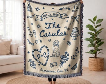 May include: Cream-colored throw blanket with navy blue illustrations and fringe. Features a banner with "AUG 23, 2026", the name "The Casulas", a heart with "P+C", a dog, and floral and celebratory icons. The text "Oconomowac Lake, WI" is also included.