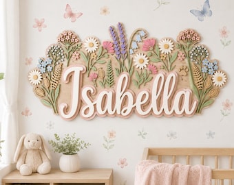 May include: A wooden wall sign featuring the name Isabella in white script lettering, layered over a natural wood background decorated with three-dimensional cutouts of colorful wildflowers, lavender sprigs, and green foliage.