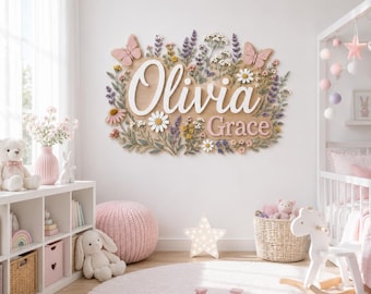 May include: A wooden wall sign featuring the name Olivia Grace in white and pink 3D lettering, surrounded by a decorative arrangement of colorful wildflowers, green foliage, and two pink butterflies, mounted on a light-colored nursery wall.