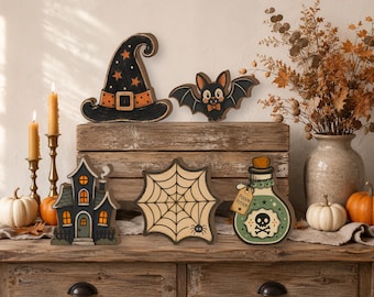 May include: A collection of wooden Halloween decorations including a black witch hat with orange stars, a bat, a haunted house, a spider web, and a green potion bottle with a skull label that reads Poison Potion, arranged on a wooden surface.