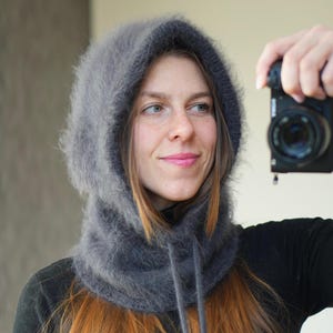 May include: A grey, fluffy hood and cowl combination with a drawstring closure. The hood is made of a soft, textured material and is designed to be worn around the head and neck. The cowl is a matching grey colour.