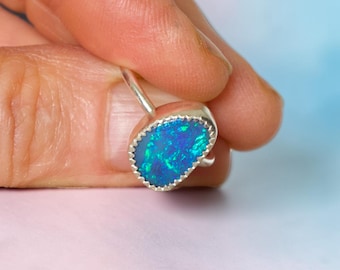 May include: A silver ring featuring an oval-shaped opal gemstone with vibrant blue and green iridescent flashes. The stone is set in a serrated metal bezel, showcasing a textured edge that secures the gem within the polished silver band structure.