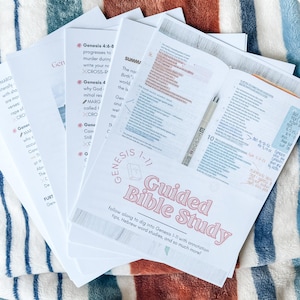 Puede incluir: Un montón de páginas de papel blanco con texto e ilustraciones, incluyendo un bolígrafo. Las páginas se titulan "Guided Bible Study" y cubren Génesis 1-11. Las páginas están sobre una manta a rayas.