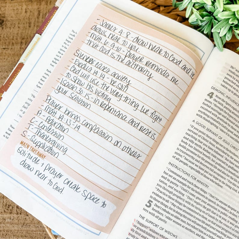May include: Open Bible with a pink sticky note featuring handwritten notes and Bible verses. The text includes phrases like "draw near to God" and "Prayer brings compassion on others." The page is open to a section with printed text.