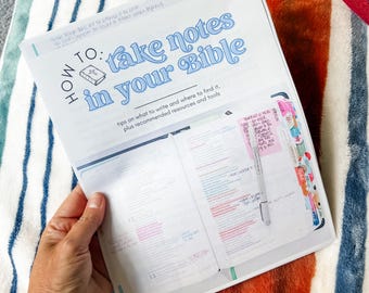 Peut inclure: Bible ouverte avec le titre "How to take notes in your Bible" en bleu. Les pages sont marquées d'onglets et de notes colorés. Un stylo est placé dans la Bible. La Bible est ouverte sur une couverture à rayures.
