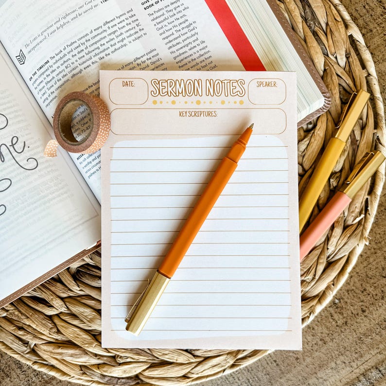 May include: A light peach-colored sermon notes pad with the words "SERMON NOTES" printed on it, along with an orange pen and several other pens. The pad has lined paper and a gold-colored pen.