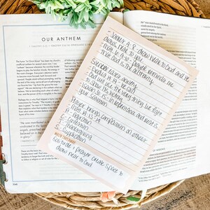 May include: A handwritten note with Bible verses and notes on a pink sticky note, resting on an open Bible. The note includes phrases like "draw near to God" and "silence eases anxiety."