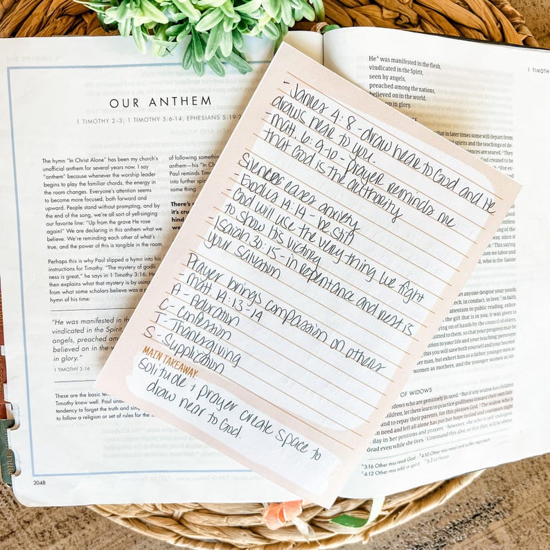 May include: A handwritten note with Bible verses and notes on a pink sticky note, resting on an open Bible. The note includes phrases like "draw near to God" and "silence eases anxiety."