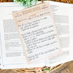 May include: A light pink sermon notes card with handwritten notes, resting on an open Bible. The card has the title "Sermon Notes" and key scripture references. The notes are in black ink.
