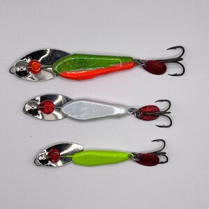 May include: Three fishing lures with silver bodies and red accents. The lures have different colored bodies: green and orange, white, and green.