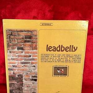 May include: A vintage vinyl record album cover for "Leadbelly" featuring a brick wall graphic on the left and a list of song titles. The album is part of the "Archive of Folk Music" collection.