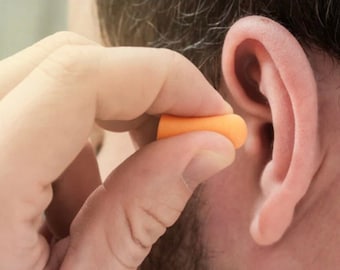 Könnte beinhalten: Eine Person, die einen leuchtend orangen Ohrstöpsel in ihr Ohr steckt.