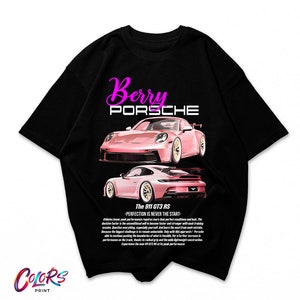 Peut inclure: T-shirt noir avec une Porsche 911 GT3 RS rose imprimée sur le devant. Le texte "Berry Porsche" est imprimé au-dessus de la voiture et le texte "The 911 GT3 RS - PERFECTION IS NEVER THE START -" est imprimé en dessous de la voiture.