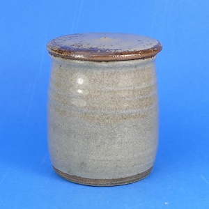 May include: A cylindrical ceramic jar with a light grey, speckled body and a smooth, dark brown lid. The jar features subtle horizontal ridges along the sides and a crackled glaze texture throughout the surface, finished with a dark brown base.
