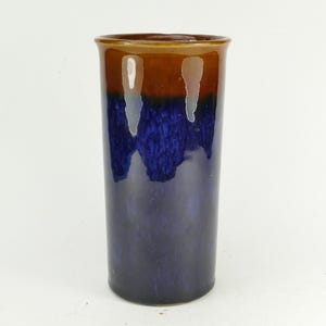 May include: A cylindrical ceramic vase featuring a glossy finish with a distinct colour transition. The upper rim and neck are glazed in a warm, earthy brown, which drips down into a deep, vibrant royal blue that covers the rest of the body.