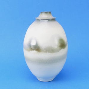 May include: A ceramic vase with an oval body and a narrow neck. The surface features a smooth white glaze with horizontal bands of muted olive green and grey mist-like gradients that wrap around the centre and the rim of the vessel.