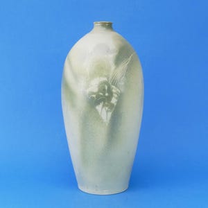 May include: A tall, oval-shaped ceramic vase with a narrow neck and a smooth, matte finish. The surface features a soft, blended gradient of off-white and muted sage green tones, with a subtle, faint floral pattern etched into the centre.