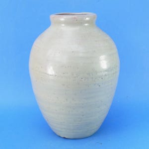 May include: A bulbous ceramic vase with a smooth, light grey glaze and a subtle speckled texture. The vessel features a rounded body that tapers towards a short, narrow neck with a thick, rolled rim, showcasing a simple, functional design.