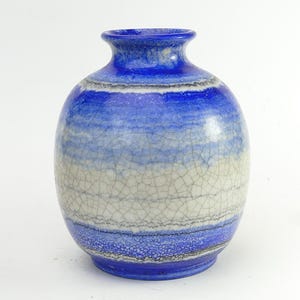 May include: A spherical ceramic vase featuring a gradient of vibrant blue at the top and bottom, transitioning to a cream-coloured centre. The entire surface is covered in a fine, dark crackle glaze pattern that creates a textured, web-like appearance.