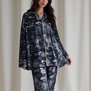 May include: Navy blue pajama set with a white and gray tropical print. The long-sleeved top and pants have white trim. The pajama set is made of a soft, comfortable material.