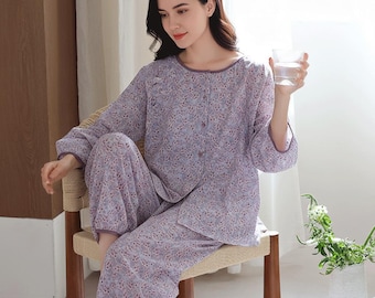 May include: A light purple floral pajama set. The long-sleeved top has a button-down front and a rounded neckline. The matching pants are loose-fitting. The set is made of a lightweight fabric, perfect for lounging or sleeping. The model is sitting on a chair.