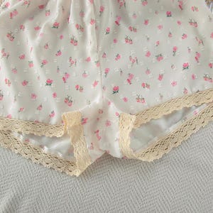 Puede incluir: Pantalones cortos blancos con estampado floral de rosas rosas y ribete de encaje crema. Estos pantalones cortos ligeros son ideales para el clima c&aacute;lido. El delicado dise&ntilde;o floral a&ntilde;ade un toque de feminidad.