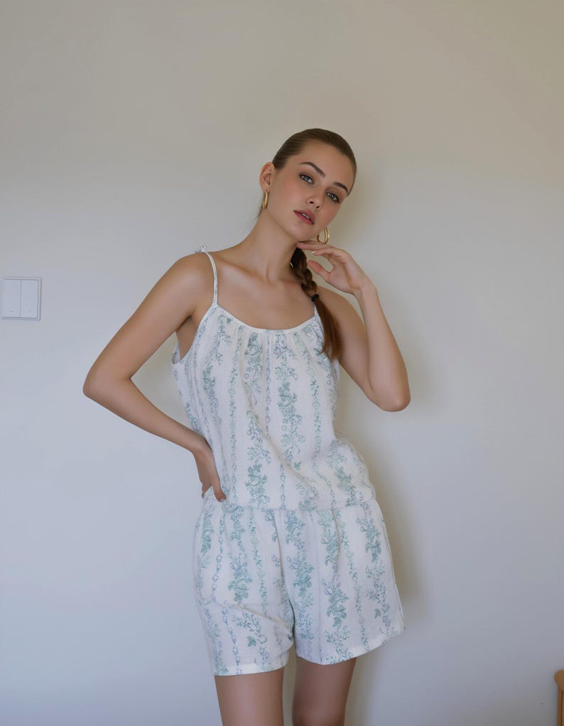 May include: A matching pajama set featuring a camisole top and shorts. The set is white with a vertical stripe pattern and a repeating floral design in a muted teal color. The camisole has thin straps.