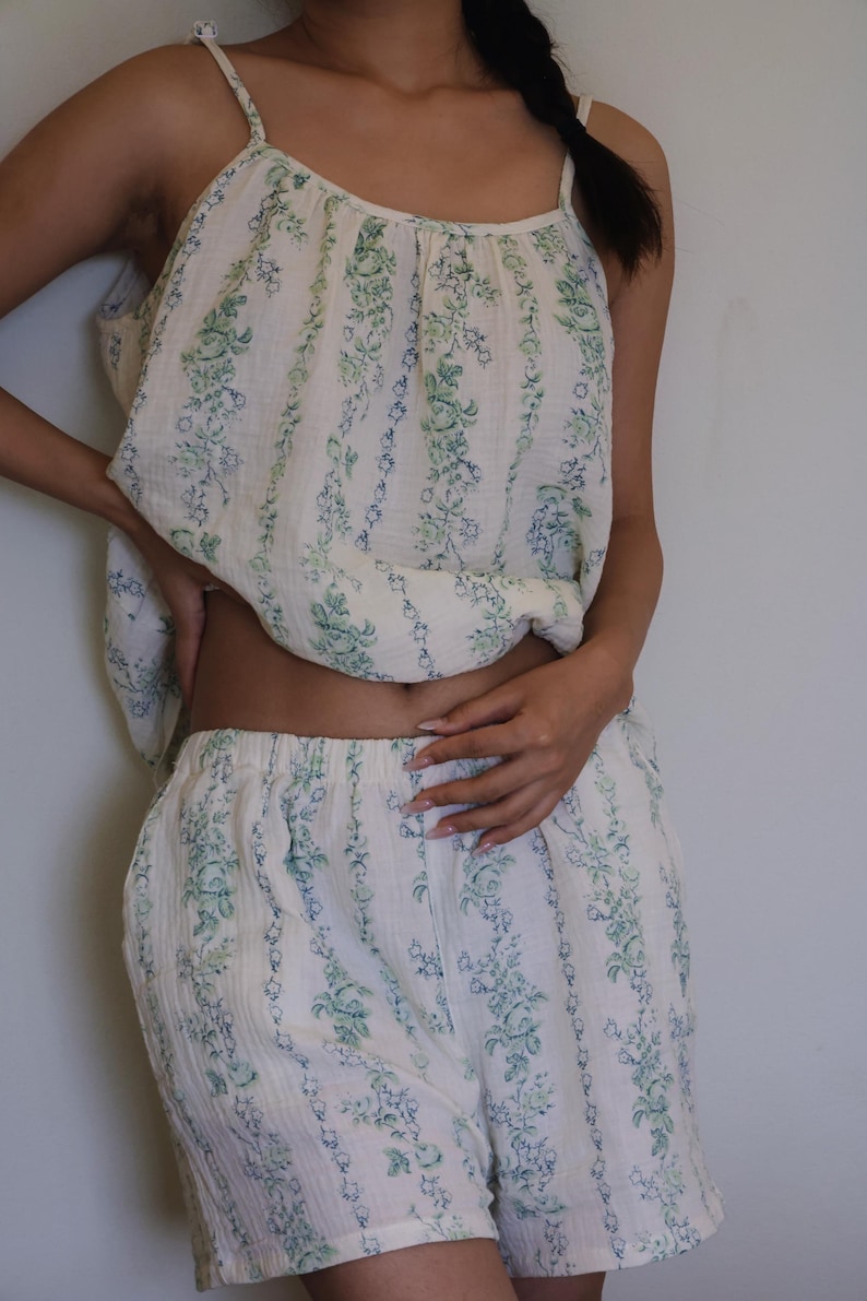 May include: A two-piece pajama set in a cream color with a vertical floral pattern in green and blue. The set includes a camisole top with thin straps and shorts. The fabric appears to be lightweight and breathable.