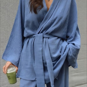 May include: A light blue, textured kimono-style top with matching pants. The top has wide sleeves and a wrap-around design with a tie belt. A person is holding a green drink in a clear cup.