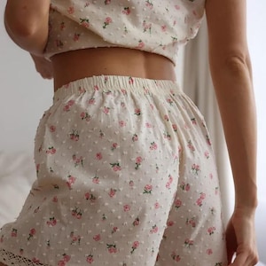Puede incluir: Conjunto de pijama color crema con estampado floral. El conjunto incluye un top corto y pantalones cortos. Los pantalones cortos tienen un ribete de encaje en la parte inferior. La tela tiene una apariencia texturizada y punteada. Rosas rosas est&aacute;n dispersas por la tela.