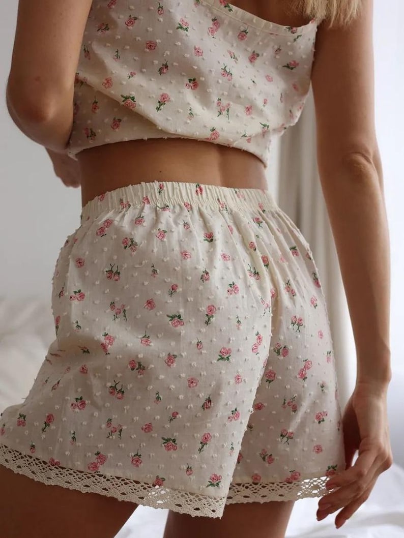 Puede incluir: Conjunto de pijama color crema con estampado floral. El conjunto incluye un top corto y pantalones cortos. Los pantalones cortos tienen un ribete de encaje en la parte inferior. La tela tiene una apariencia texturizada y punteada. Rosas rosas est&aacute;n dispersas por la tela.