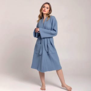 May include: A light blue robe with long sleeves, a tie belt, and two front pockets. The robe is knee-length and made of a soft, textured fabric. The model is wearing the robe.