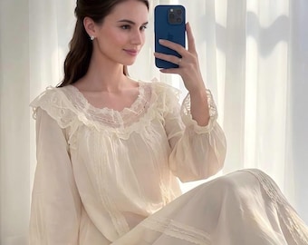 May include: A long-sleeved cream-colored nightgown featuring a ruffled neckline, delicate lace trim along the collar and cuffs, and vertical lace paneling down the front. The garment is made of a lightweight, semi-sheer fabric with a loose, flowing fit.