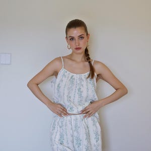 May include: A white pajama set with a green floral pattern. The set includes a camisole top with thin straps and matching shorts. The fabric has vertical stripes. The model is wearing gold hoop earrings.