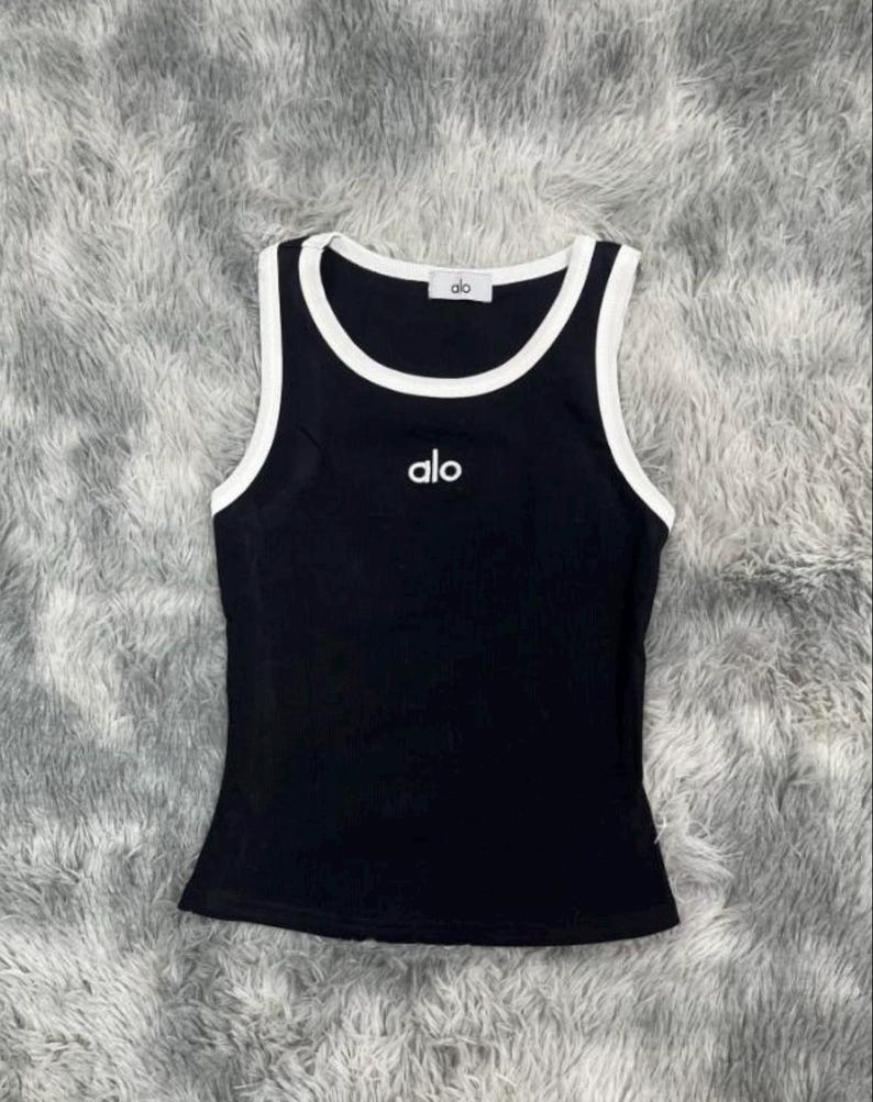 Może przedstawiać: Biały ceramiczny kubek z czarnym uchem i napisem "But First, Coffee" w stylu odręcznym. Kubek stoi na białej powierzchni. Kubek ma około 10 cm wysokości.