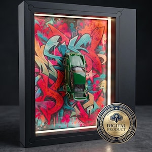 May include: A dark green toy sports car mounted inside a black rectangular shadow box frame. The background features a vibrant graffiti art print with red, pink, and teal spray paint patterns. A gold circular seal reads DIGITAL PRODUCT.