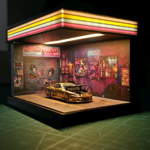 Puede incluir: Diorama en miniatura de un coche deportivo dorado con el capó abierto, estacionado en un garaje iluminado con neón. La escena incluye letreros que dicen "NEO-TOKYO CUSTOMS" y "OPEN 24/7", con carteles coloridos y estética retro.