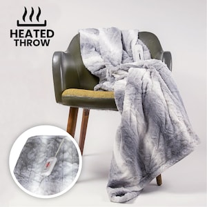 May include: A gray and white faux fur heated throw blanket draped over a green chair. The blanket has a control panel with a red light. The words "HEATED THROW" are printed in black above the chair.