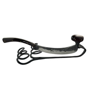 May include: A black metal knife with a wooden handle and a curved blade. The knife is attached to a black metal stand with a decorative scroll design.