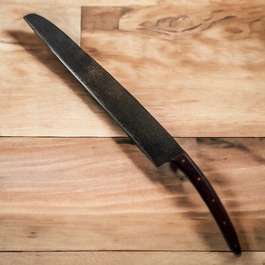 May include: A long, black,  knife with a wooden handle. The blade is slightly curved and has a textured finish. The handle is dark brown with a slight reddish hue.