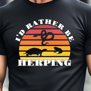 May include: Black t-shirt with a retro sunset graphic and the text "I'd Rather Be Herping". The graphic features a snake, a turtle, and a frog.