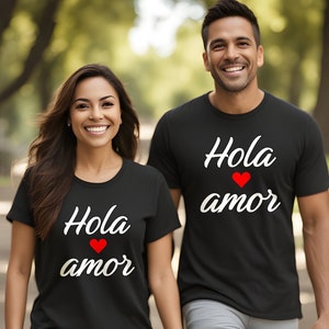 May include: A couple wearing matching black t-shirts with the text "Hola amor" and a red heart. The shirts are a matching couple's set.